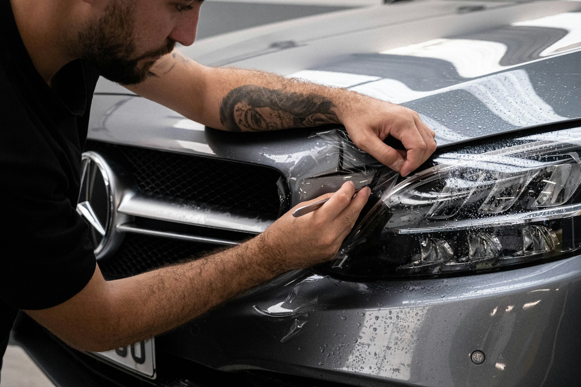 Detailer pracujacy przy reflektorze i lakierze srebrnego samochodu